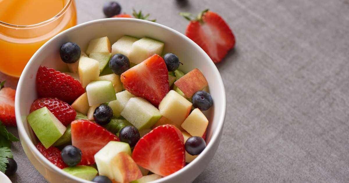  A bowl containing fresh strawberries, blueberries, apples, and orange juice in the background.